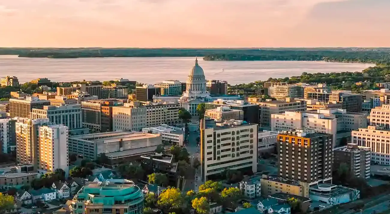 Aerial view of downtown Madison, Wisconsin at sunset, showcasing the Wisconsin State Capitol surrounded by buildings, lakes, and tree-lined streets.