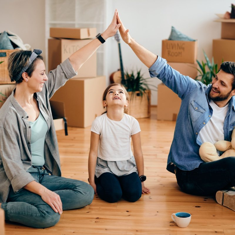 happy-family-after-buying-madison-home A happy family sits on the floor surrounded by moving boxes, smiling and giving a high-five to celebrate moving into their new home.